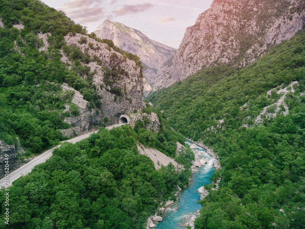 Obraz premium Winding road following Moraca river in a deep green valley with a tunnel cutting through the rugged mountain and rocky terrain in Montenegro