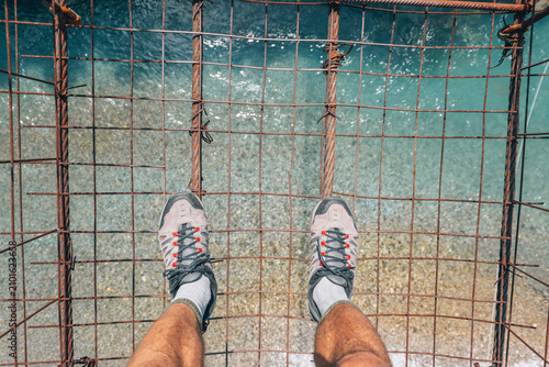 Foto Adventurer is standing on a shaky old suspension bridge, looking down at the cle