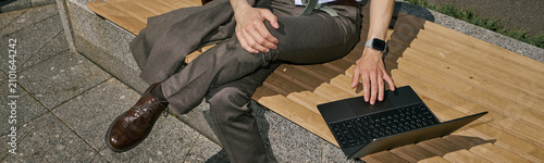 Canvastavla Young adult businessman sitting on outdoor bench and using laptop, working remotely during commute