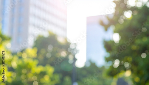 Blurred background with modern city buildings surrounded by lush green trees, warm sunlight filtering through foliage, soft bokeh effect, contemporary urban lifestyle concept.