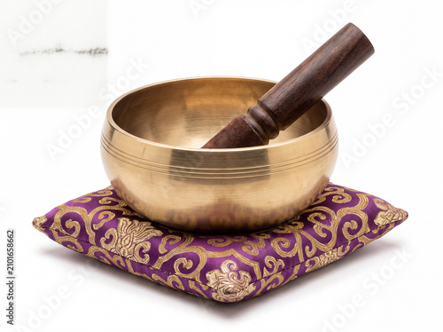 Tibetan brass singing bowl with wooden mallet on purple embroidered cushion for sound healing
