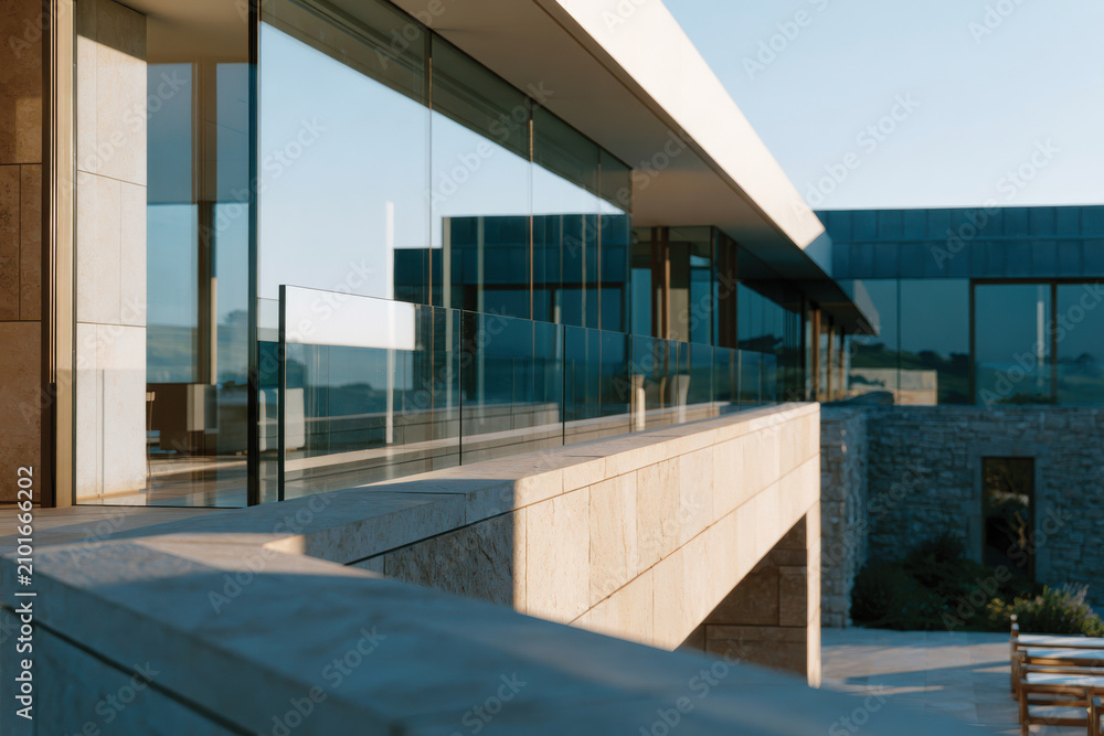 Fototapeta premium Modern architecture features sleek glass panels and stone elements, reflecting a harmonious blend of nature and innovative design under clear blue skies.