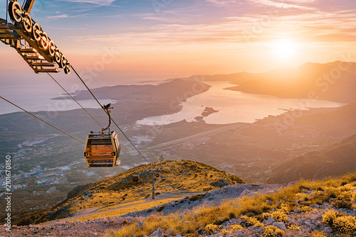 Fotografi Cable car ascending rugged mountain slope with a dramatic sunset illuminating th