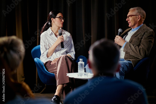 Fotografie Medium shot of Caucasian businesswoman and senior man speaking on stage during panel discussion, sharing expertise and leadership insights