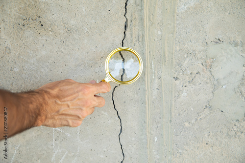 Male hand with a magnifying glass checking a cracked wall after earthquake.