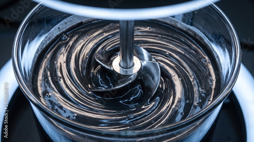 Close up of a metal impeller stirring dark viscous electrode slurry for battery production