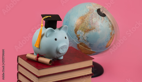 Принти на полотні A conceptual composition about the cost of education, featuring a graduate's mortarboard, a piggy bank, books, a scroll, and a globe against a pink background