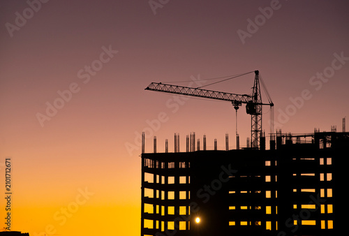 Silhouette of a building under construction with cranes at sunset