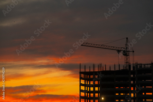 Silhouette of a building under construction with cranes at sunset