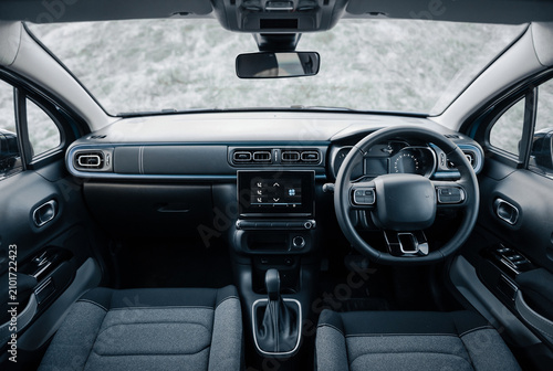 Right-hand drive compact car interior with blue accents. Interior of compact hatchback by snow pile: front panel with dashboard and steering wheel.