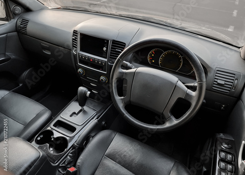 Cockpit of an old SUV with black leathers seats. Steering wheel and dashboard of mid 2000s SUV in parking lot. 