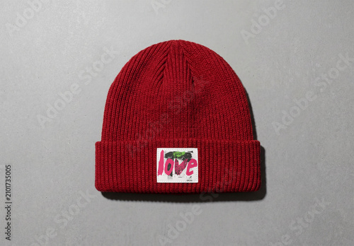 Mockup of A red beanie cap with white label sits flat on a grey surface