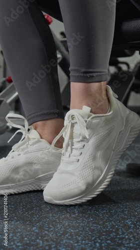 Vertical close up video of young Caucasian woman tying laces of sneakers in gym. Footage for fitness apps, sportswear commercials, and healthy lifestyle marketing campaigns