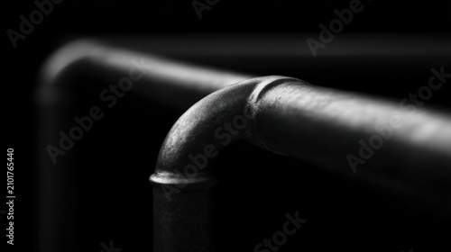 Close up of a curved metallic pipe in monochrome with a dark background