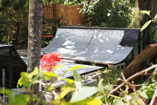 Skate ramp made from iron in an outdoor area with plants around it during a sunny day.