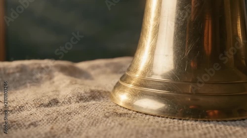 Brass bell with wooden handle placed on burlap fabric surface. Macro view of metal instrument reflecting morning light. Handbell for classroom or service signal
