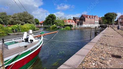 Historic harbor in Ribe with a traditional sailing ship, cobblestone promenade and historic waterfront buildings on a sunny summer day.