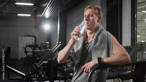 Young man drinking water and wiping sweat with towel in gym. Clip for fitness app marketing, hydration campaigns, and wellness advertisements