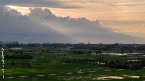 Sunbeams pierce dramatic clouds. Golden hour light softens the scene. Sunlight glint on green fields
