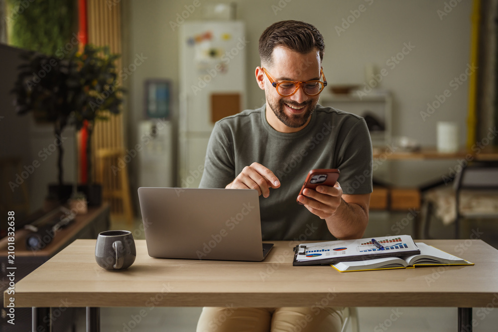 Obraz premium Smiling man using smartphone and laptop working from home