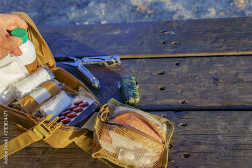 Person opening a tactical first aid kit on a wooden surface, showing essential medical items, a multitool, and a lighter
