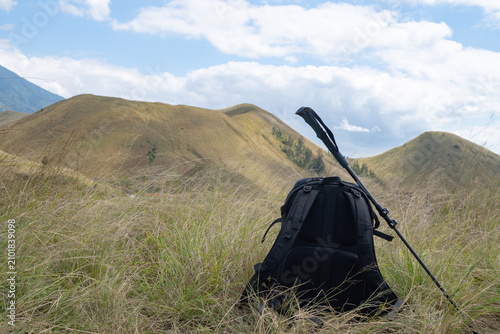 Serene Mountain Landscape with Hiking Backpack, Pole, and Expansive Green Hills Under Blue Sky