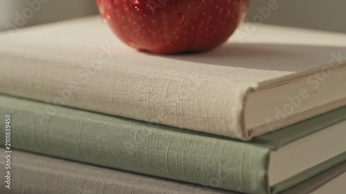 Red apple covered in water drops resting on a stack of linen bound books. Still life composition featuring fruit, literature and educational reading material concept