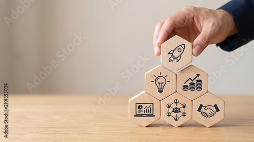 A hand placing a rocket icon block on a pyramid of business strategy and growth concepts, symbolizing innovation and success.