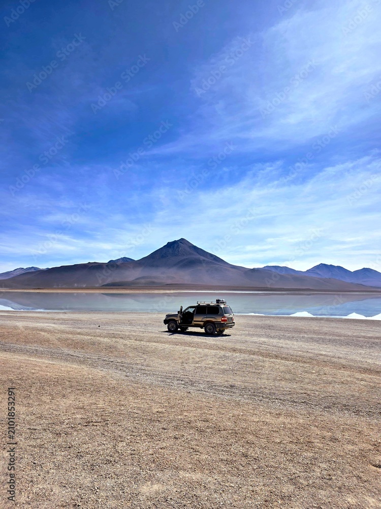Obraz premium Off‑road vehicle parked in a remote desert landscape near a reflective lake