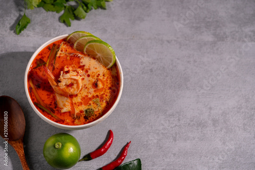 Spicy Thai seafood soup served in a white bowl with shrimp, squid, lime, chili, and fresh herbs on a wooden table, traditional Asian cuisine concept.