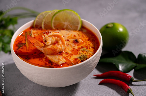 Spicy Thai seafood soup served in a white bowl with shrimp, squid, lime, chili, and fresh herbs on a wooden table, traditional Asian cuisine concept.