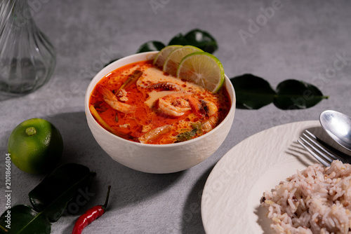 Spicy Thai seafood soup served in a white bowl with shrimp, squid, lime, chili, and fresh herbs on a wooden table, traditional Asian cuisine concept.