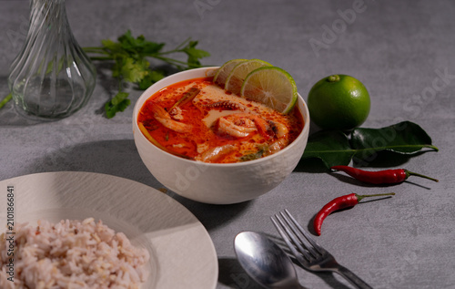 Spicy Thai seafood soup served in a white bowl with shrimp, squid, lime, chili, and fresh herbs on a wooden table, traditional Asian cuisine concept.