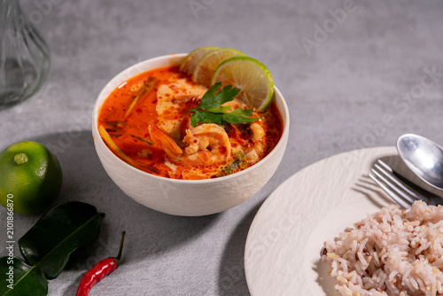 Spicy Thai seafood soup served in a white bowl with shrimp, squid, lime, chili, and fresh herbs on a wooden table, traditional Asian cuisine concept.