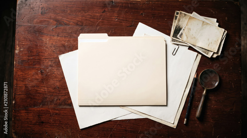 Clean overhead shot of a vintage desk with a blank folder, old photos, and a magnifying glass.