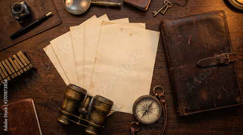 Flat lay of a vintage spy's desk with blank aged papers, binoculars, compass, and leather journal.
