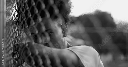Fotografi Latin Hispanic man of African descent resting head and arm against fence, gazing