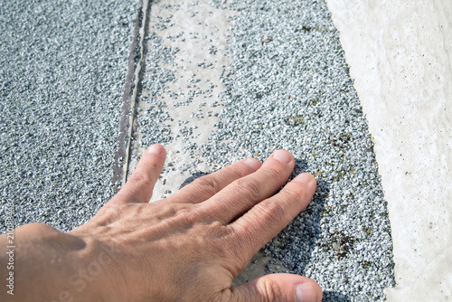 Flat roof granule loss inspected by roofer. Bare spot on aged modified bitumen cap sheet at concrete parapet edge. UV degradation risk. 2-ply SBS or modified bitumen roofing system. Selective focus.