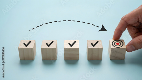 Hand placing a wooden block with target icon representing goal achievement business planning strategy management completion development improvement milestone