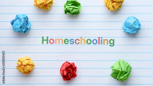 A lined notebook page featuring the word Homeschooling printed in colorful letters, surrounded by paper crumpled balls. Close up.