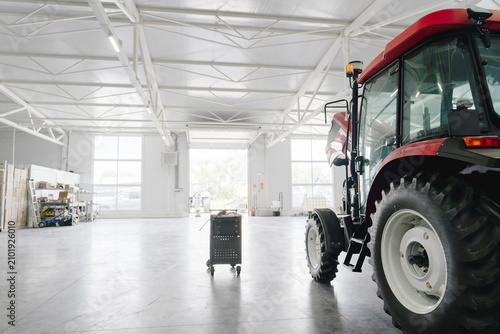Modern agricultural tractor in spacious service workshop, professional farm equipment maintenance, industrial repair facility with copy space, agriculture technology.