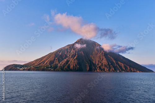 Scenic view of the active volcanic cone of Stromboli rising from the sea at sunset with pink clouds