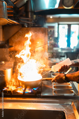Konstfotografi Culinary Mastery in Action: A chef's skilled hands orchestrate a fiery culinary creation in a professional kitchen, showcasing the intense heat and dynamic atmosphere of a busy restaurant