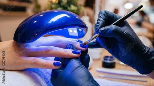 Nail technician applying blue gel polish under UV lamp