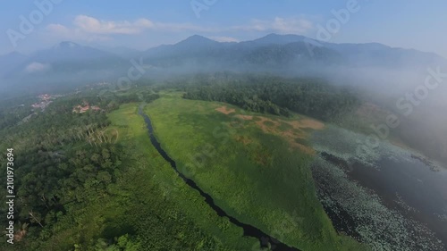 Aerial fisheye view mist hugs mountain peaks. Green rivers wind through lush valleys. Fog drifts low over dense forests