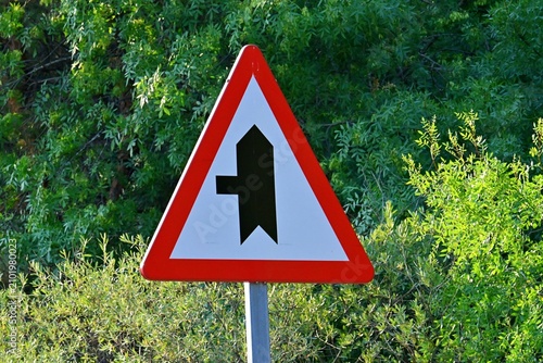 Warning road sign signaling a road merge from the left onto the main traffic lane. July 13, 2026