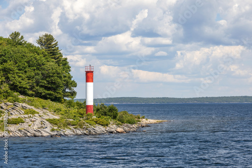 Red and white lighthouse on rocky shoreline of Killbear Provincial Park, seen from Parry Sound's 30,000 Islands Cruise in Ontario.