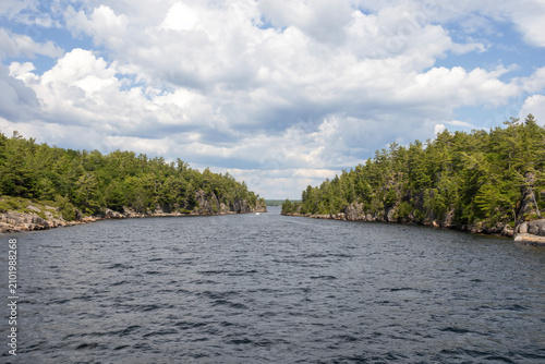 A distant view of Hole in the Wall from the 30,000 Islands cruise in Parry Sound, Ontario, showcasing lush greenery and serene waters under a partly cloudy sky.