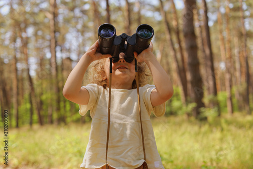 Canvas Print A child stands in a forest holding binoculars, observing the surroundings with interest