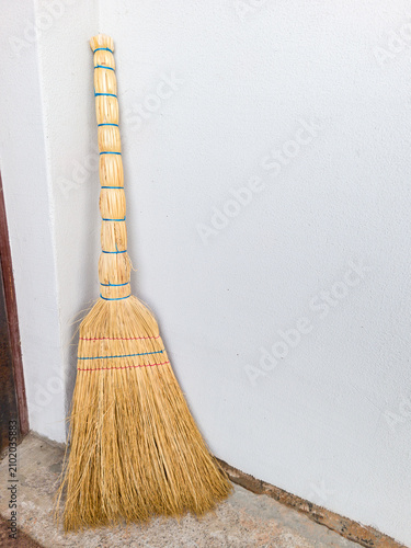 Traditional sorghum straw broom standing against white wall